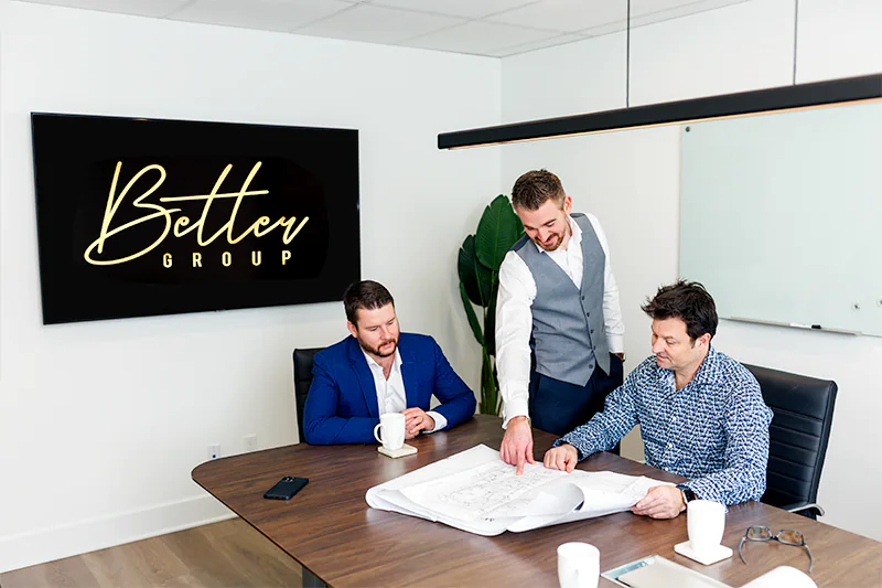 Three business partners review building plans during their team meeting.  A commercial photo by Jeffrey Meyer.
